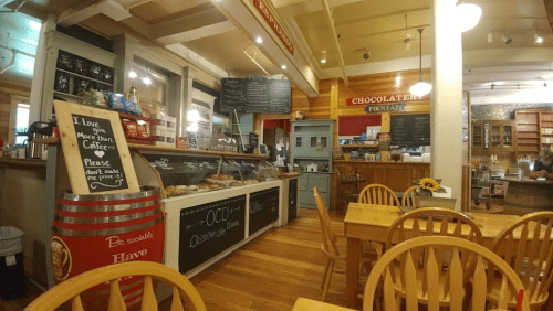 Cozy café interior with wooden tables, a display case of pastries, and a chalkboard menu in a warm, inviting atmosphere.