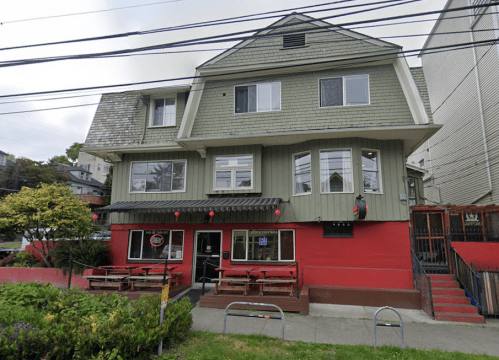 A two-story building with a green and red exterior, featuring outdoor seating and large windows.