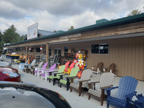 A storefront with colorful Adirondack chairs outside, surrounded by various outdoor furniture and decorations.