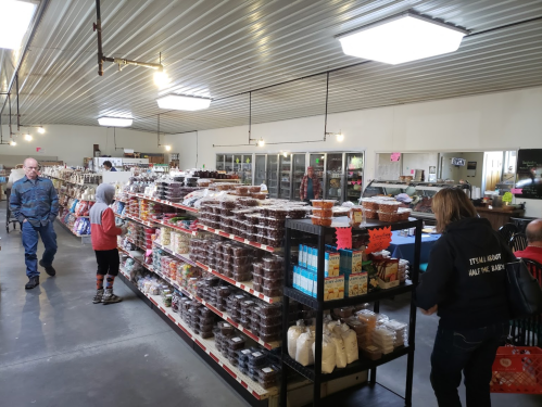 A spacious market interior with shelves of packaged goods, shoppers browsing, and a variety of products on display.