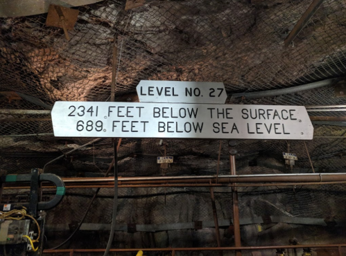 Sign indicating "Level No. 27: 2341 feet below the surface, 689 feet below sea level" in a mine.