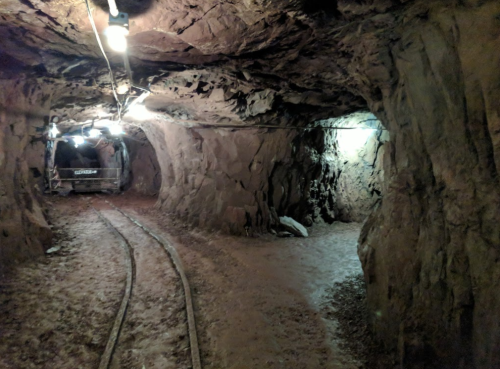 A dimly lit underground mine tunnel with rocky walls and tracks for a mining cart.