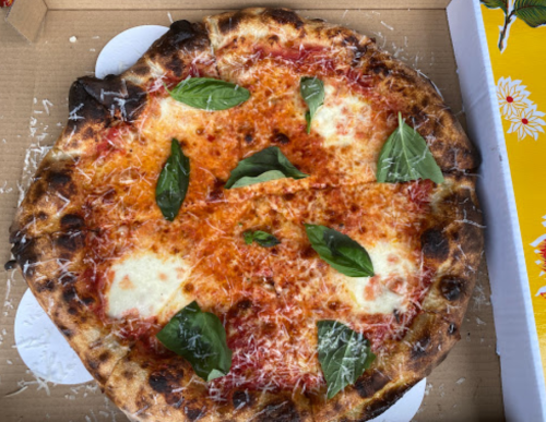 A freshly baked pizza topped with mozzarella, tomato sauce, fresh basil, and grated cheese, in a pizza box.