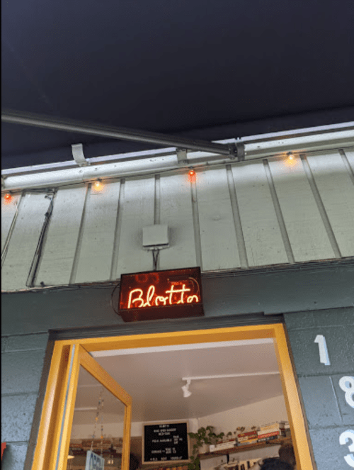 Neon sign reading "Blotto" above an open door, with a cozy interior visible.
