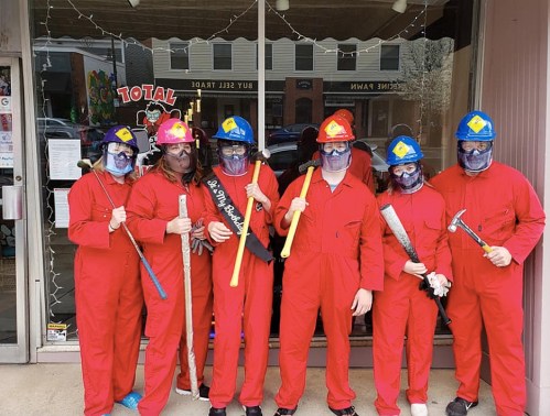 A group of six people in red jumpsuits and helmets, holding various tools, posing outside a store.