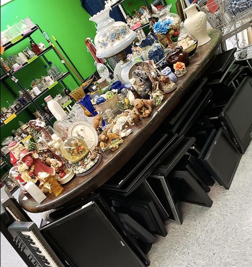 A cluttered table filled with various decorative items and collectibles, surrounded by stacked black chairs.