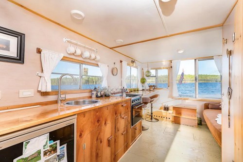 Cozy kitchen with wooden cabinets, sink, stove, and large windows overlooking a scenic lake view.