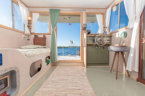 Cozy interior of a boat with a bed, steering wheel, and large windows overlooking the water.