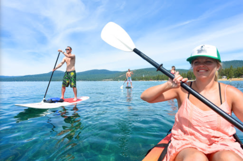 A group of people paddleboarding on a clear lake on a sunny day, with mountains in the background.