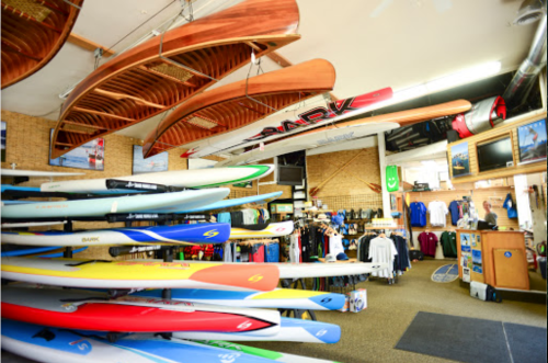 A vibrant sports shop interior showcasing various kayaks, paddleboards, and apparel on display.