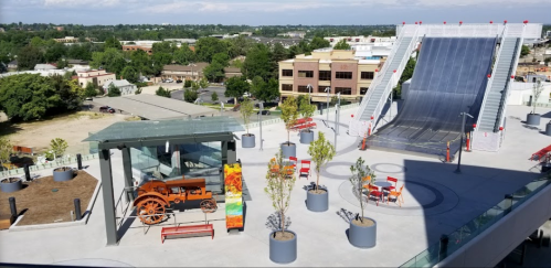 A rooftop area featuring an old tractor, seating, trees, and a large ramp, with a cityscape in the background.