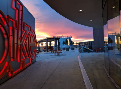 A vibrant sunset casts colorful hues over a modern outdoor space with seating and illuminated signage.