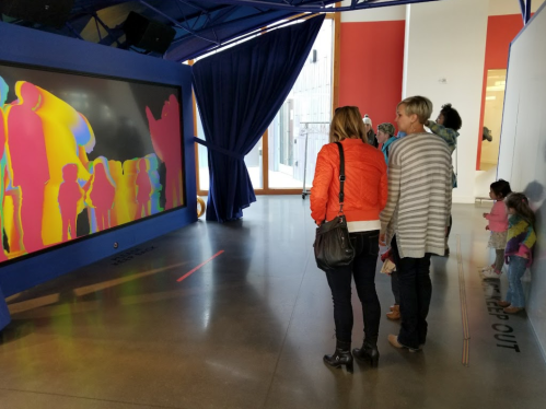 Two adults and a child observe a colorful, abstract art installation in a modern gallery space.
