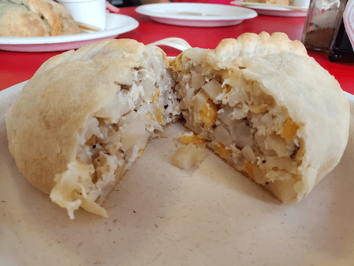A cut-open pastry revealing a filling of potatoes, chicken, and vegetables on a white plate.