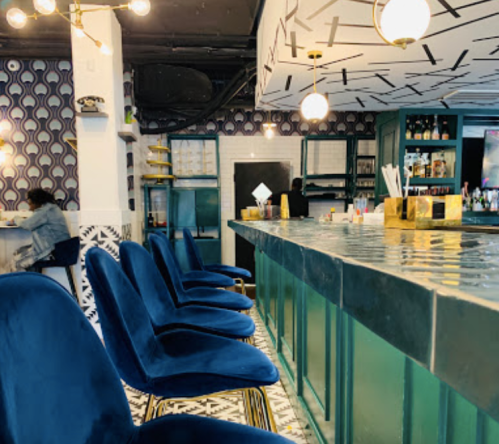 A stylish bar with blue velvet chairs, patterned walls, and a modern counter, creating a vibrant atmosphere.