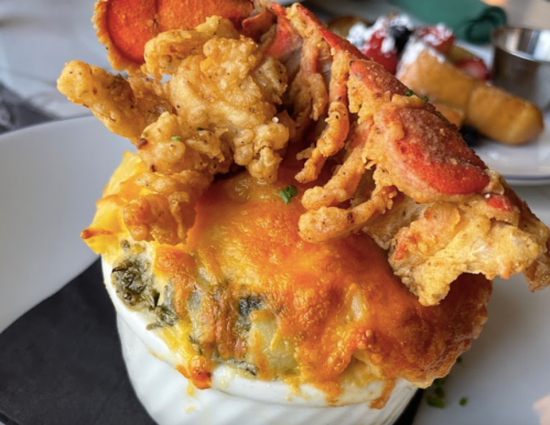 A close-up of a creamy dish topped with lobster and fried chicken, garnished with herbs on a white plate.