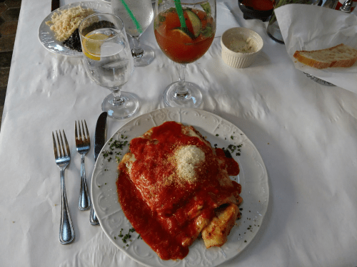 A plate of pasta topped with marinara sauce and cheese, accompanied by drinks and bread on a table setting.