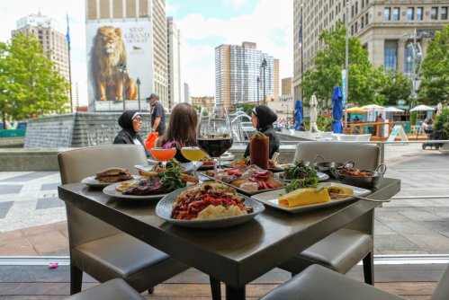 A table filled with various dishes and drinks, with a cityscape and people in the background.