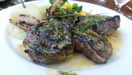 A plate of grilled lamb chops topped with herbs, served with mashed potatoes and mixed vegetables.