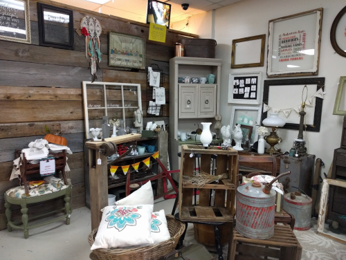 A cozy vintage shop display featuring wooden furniture, decor items, and various antiques arranged on shelves and tables.