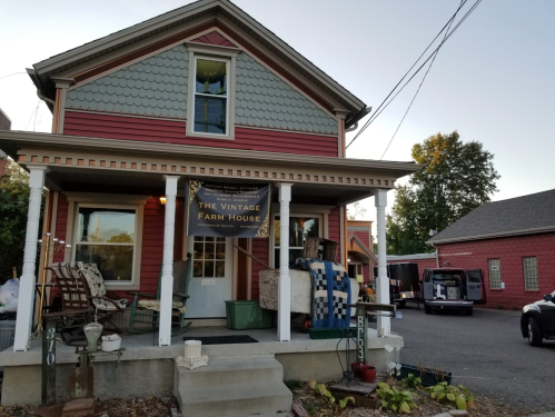 A charming red and blue vintage house with a sign reading "The Vintage Farm House" and a porch filled with furniture.