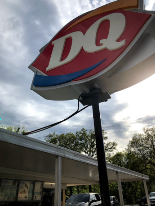Sign for Dairy Queen (DQ) with a cloudy sky in the background and a building structure below.