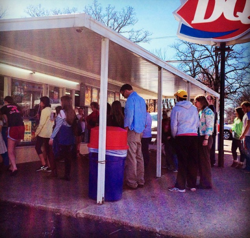 A crowd of people gathered outside a Dairy Queen, enjoying a sunny day.