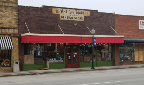 A vintage-style storefront with a red awning, labeled "The Antique Market," featuring large windows and a green base.