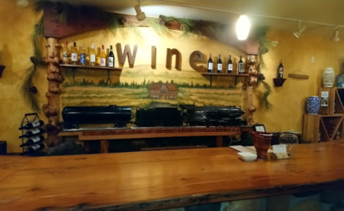 A rustic wine bar with a wooden counter, shelves of wine bottles, and a mural of a vineyard in the background.