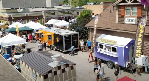 A bustling outdoor market with food trucks, tents, and people enjoying the sunny day.
