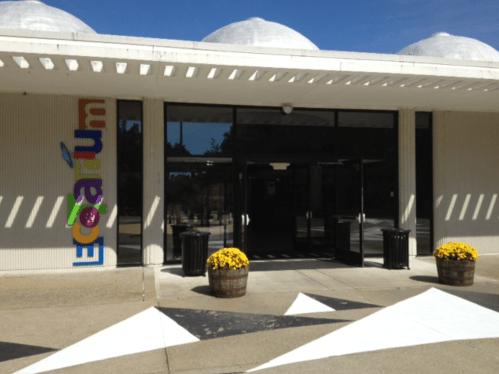 Entrance of an aquarium building with colorful signage and flower pots on the sidewalk.