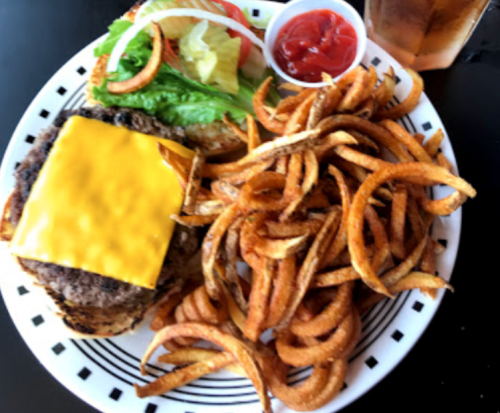 A plate featuring a cheeseburger with lettuce and tomato, accompanied by curly fries and dipping sauces.