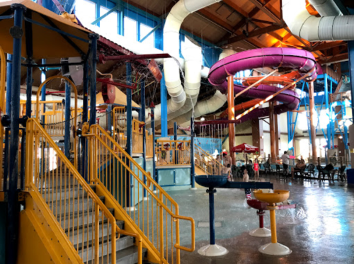 Indoor water park featuring colorful slides, play structures, and a spacious seating area. Bright and inviting atmosphere.
