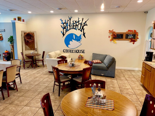 Cozy coffee house interior with tables, chairs, and a blue fox mural on the wall. Warm, inviting atmosphere.
