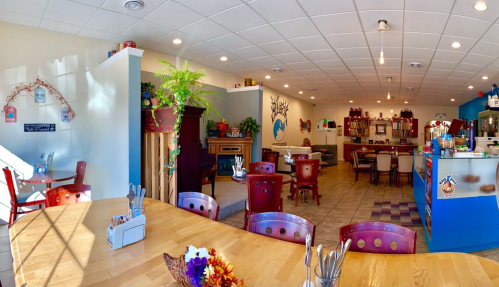 Cozy restaurant interior with wooden tables, colorful decor, and a welcoming atmosphere. Plants and artwork enhance the space.