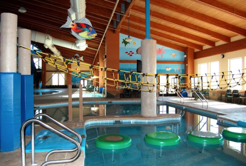 Indoor pool area featuring floating green rings, a rope bridge, and colorful underwater-themed murals on the walls.