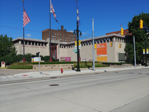 Exterior view of the Detroit Historical Museum with flags and signage, set against a clear blue sky.