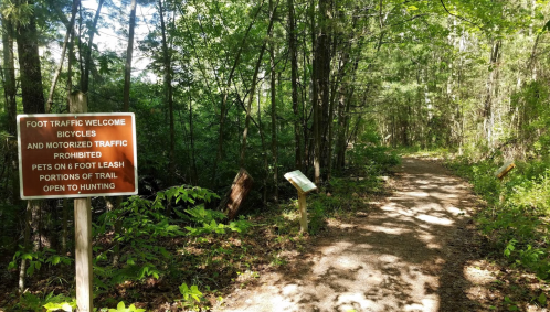 A wooded trail with signs indicating foot traffic is welcome, but bicycles and motorized traffic are prohibited.