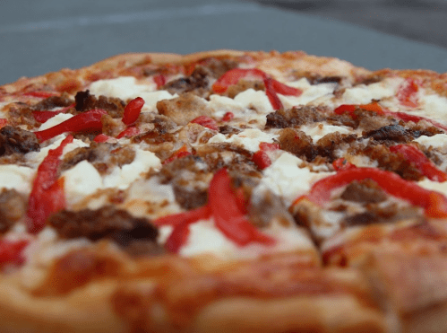 Close-up of a pizza topped with ground meat, red peppers, and cheese on a golden crust.