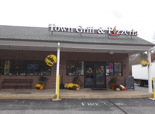Exterior of Town Grill & Pizzeria featuring a sign, flowers, and a welcoming entrance on a cloudy day.