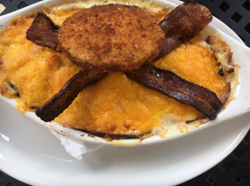 A baked dish topped with melted cheese, crispy bacon, and a golden-brown patty, served in a white dish.