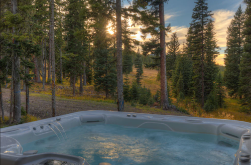 A hot tub surrounded by trees, with a sunset illuminating the forest in the background.