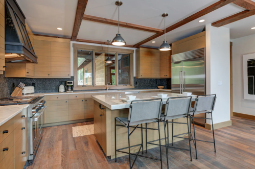 Modern kitchen with wooden beams, sleek cabinetry, a large island, and bar stools, featuring stainless steel appliances.