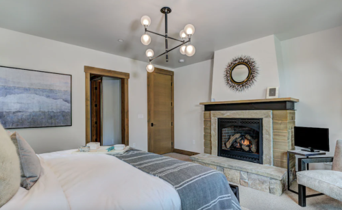 Cozy bedroom featuring a fireplace, modern chandelier, and artwork, with a neutral color palette and soft furnishings.