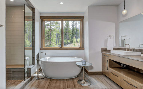 Modern bathroom featuring a freestanding tub, wooden vanity, and large window with a forest view.