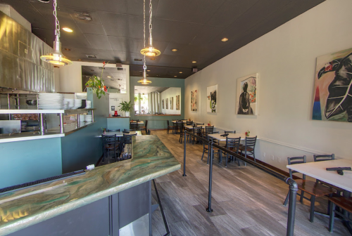 Interior of a modern restaurant featuring a bar, tables, and colorful artwork on the walls. Bright and inviting atmosphere.