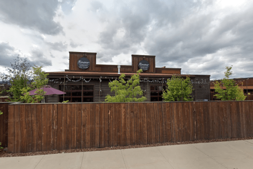 A wooden building with a sign reading "Riverton" surrounded by trees and a wooden fence, under a cloudy sky.