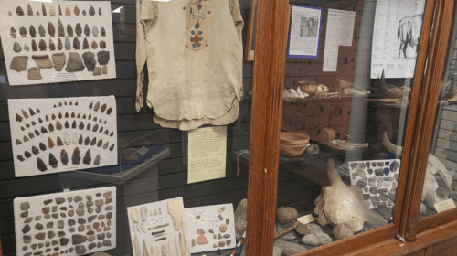 Display case featuring various artifacts, including tools, clothing, and historical items from different cultures.
