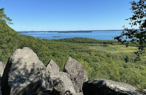 A scenic view of a lush green landscape with a calm blue lake and distant islands under a clear blue sky.