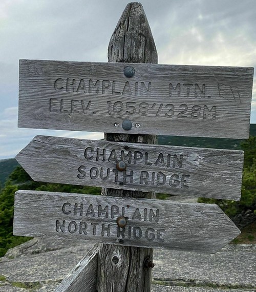 Wooden signpost with directional arrows for Champlain Mountain trails: South Ridge and North Ridge, elevation 1956 ft.